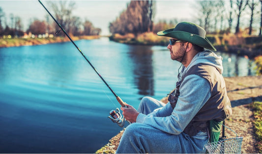 Man wearing polarized sunglasses and a wide-brim hat fishing by a calm river